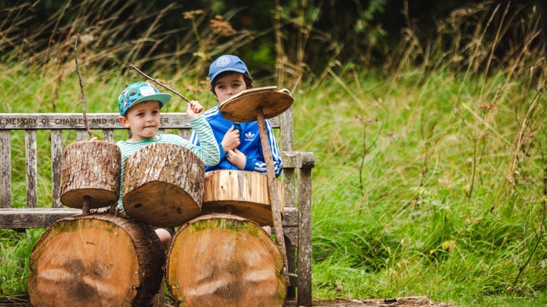 Children play natural instruments in the log stack at Dyffryn Gardens, Vale of Glamorgan